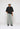 Eine Person, die ein schwarzes Poloshirt, Island Blue Eightyfive Dividing Seam Jeans und eine weiße Mütze trägt, steht vor einem schlichten Hintergrund.