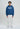 Eine Person blickt nach vorne und trägt den LowLights Shutter Zip Hoodie navy von LowLights Men, gestylt mit weißer Hose und Turnschuhen, vor einem schlichten hellen Hintergrund.