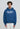 Eine Person, die einen LowLights Men LowLights Shutter Zip Hoodie in Marineblau mit dem Schriftzug "Low-Light Studios" auf der Vorderseite und eine weiße Hose trägt, steht vor einem einfarbigen Hintergrund.