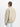 Eine Person mit geflochtenen Haaren steht mit dem Gesicht zur Wand und trägt eine beigefarbene Bio-Jacke MA-1 Heritage von Alpha Industries über einem grünen Hemd und hellblaue Jeans vor einem schlichten weißen Hintergrund.