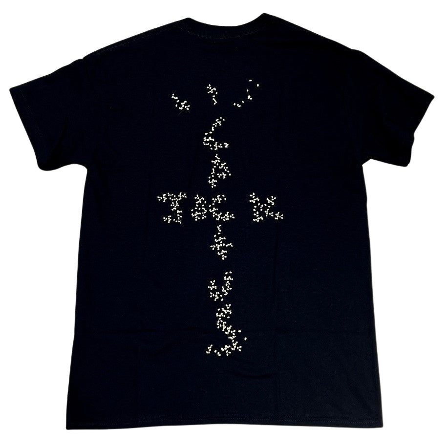 Schwarzes Travis Scott x McDonald's Sesame II-T-Shirt mit einem weißen abstrakten Splatterdesign, das einem vertikalen linearen Muster ähnelt, inspiriert von Travis Scott, dargestellt auf einem einfarbigen Hintergrund.
