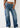 Eine Person in locker sitzenden True Religion Bobbi Baggy Jeans Dark Wash, einem weißen Crop Top und weißen Schuhen steht vor einem schlichten hellen Hintergrund.