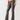 Eine Person, die True Religion Joey LR Bootcut Flap Charcoal-Jeans mit durchsichtigen, hochhackigen Sandalen und einem abgeschnittenen Oberteil trägt, steht vor einem schlichten Hintergrund.